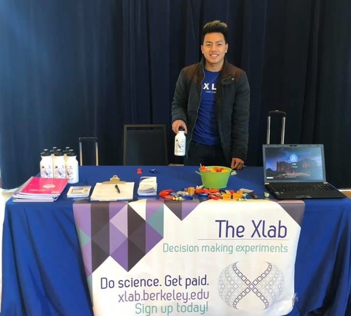 Xlab student worker at Crossroads with an Xlan banner and fliers